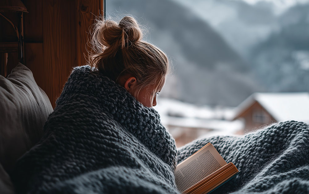 Young woman sitting by a window wrapped in a blanket, reflecting on pregnancy and adoption options