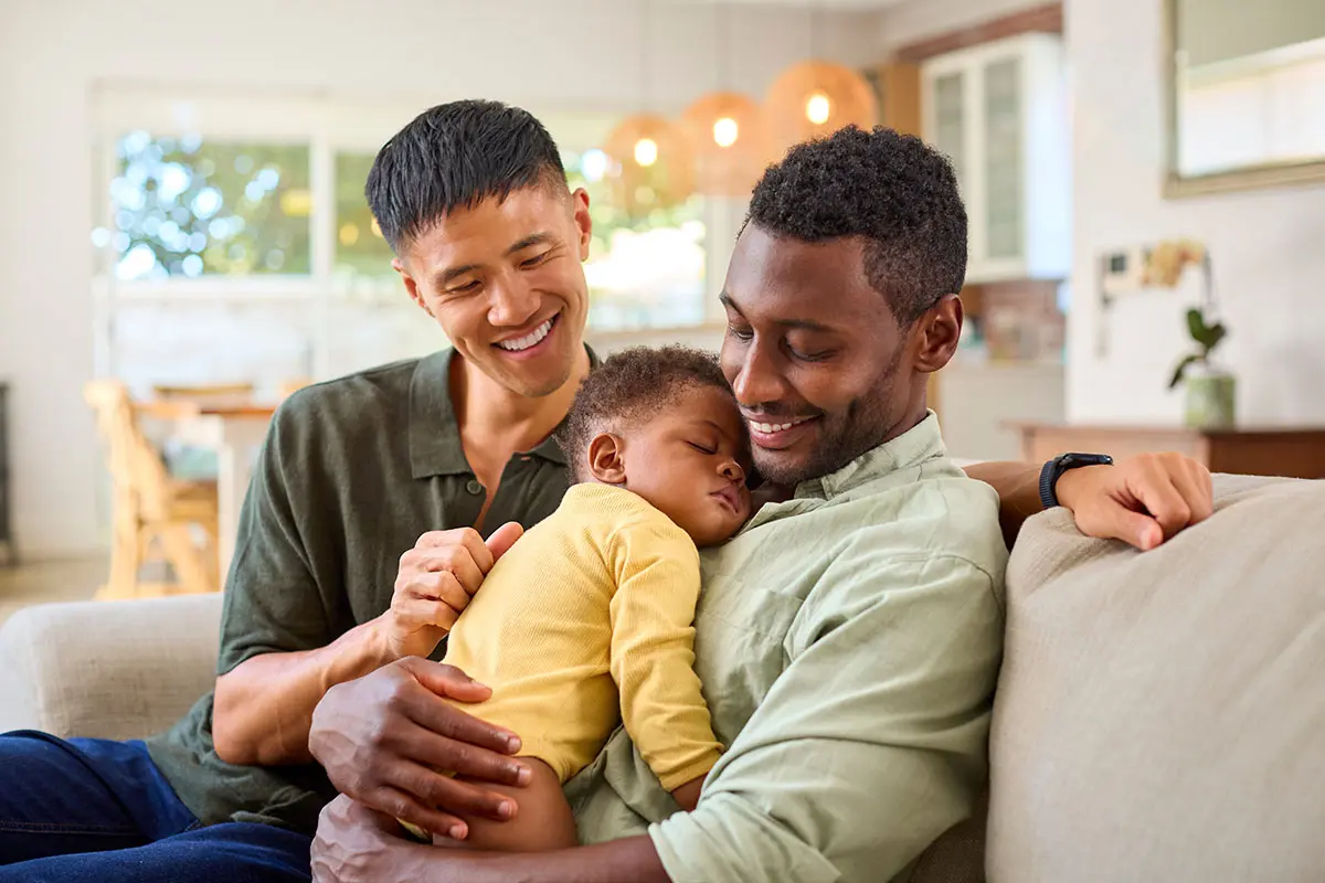 Two adoptive fathers holding their child, illustrating the lifelong benefits of open adoption and strong family connections.
